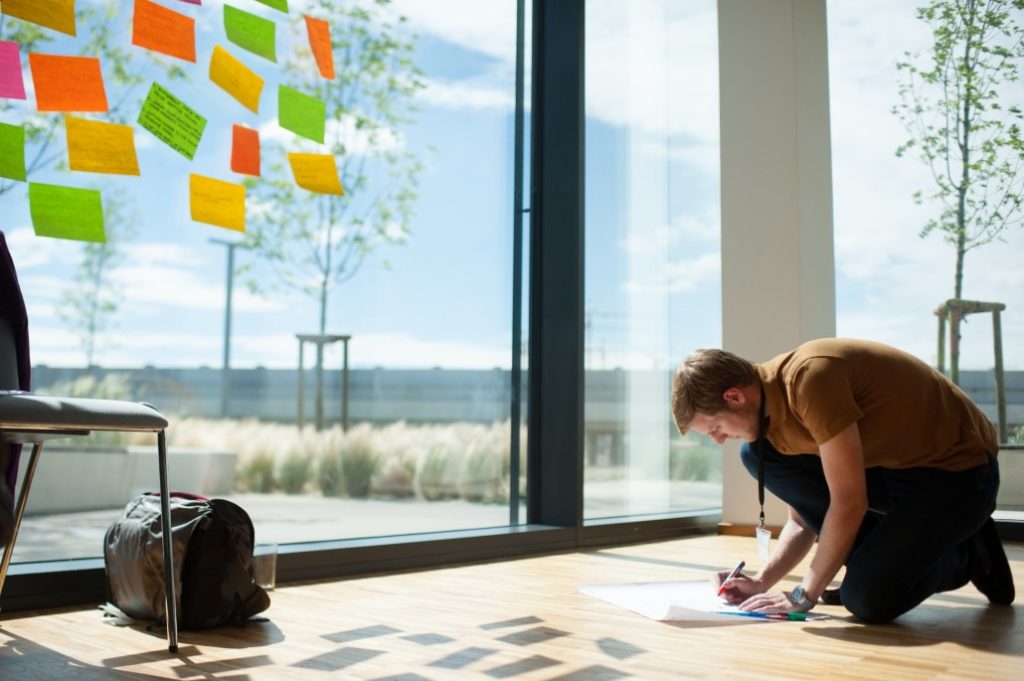 A man writing on a poster while kneeling on the ground, working on his social or environmental company