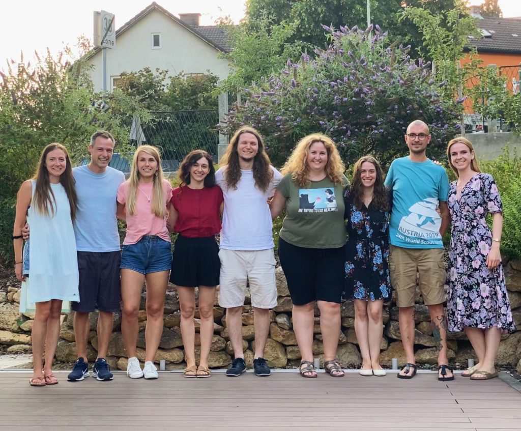 A team of men and women standing next to each other, posing for a photo in a garden.